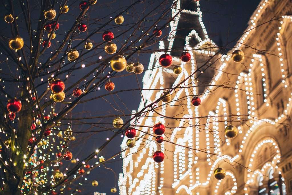 5 Christmas Traditions You Should Start with Your Kids 6 christmas ornaments in a tree and a building decorated with christmas lights