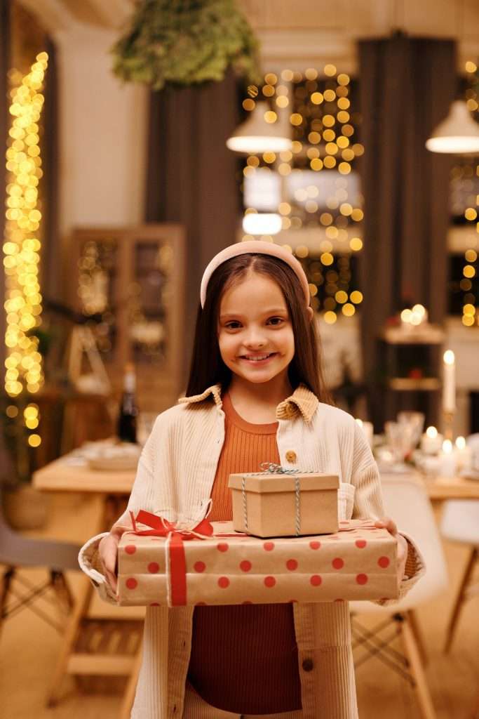 5 Christmas Traditions You Should Start with Your Kids 7 little girl holding christmas presents and smiling