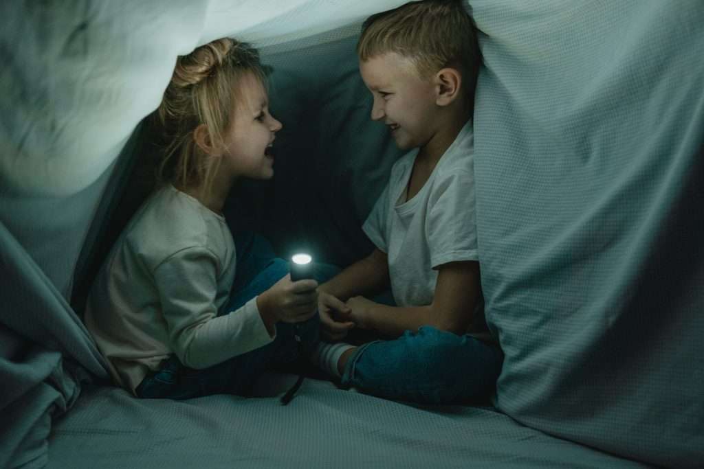 little girl and little boy playing under the covers with a flashlight
