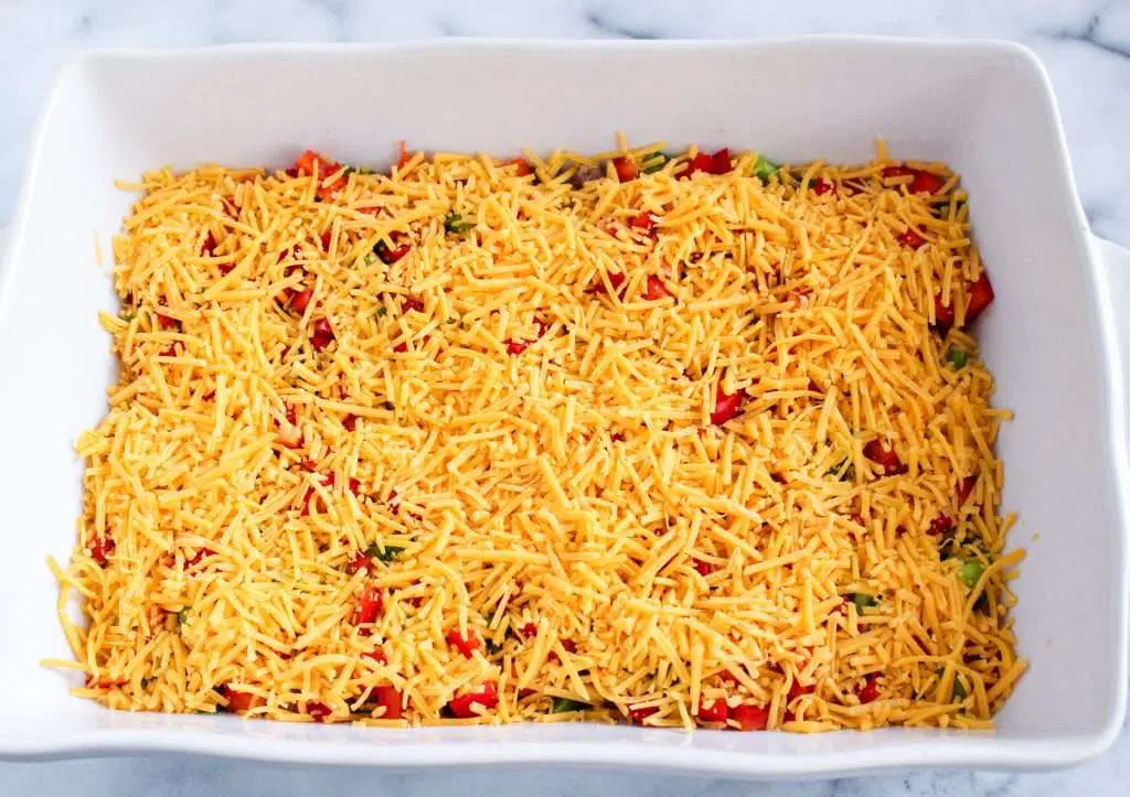 diced peppers and sausage in white baking dish with cheese on top 