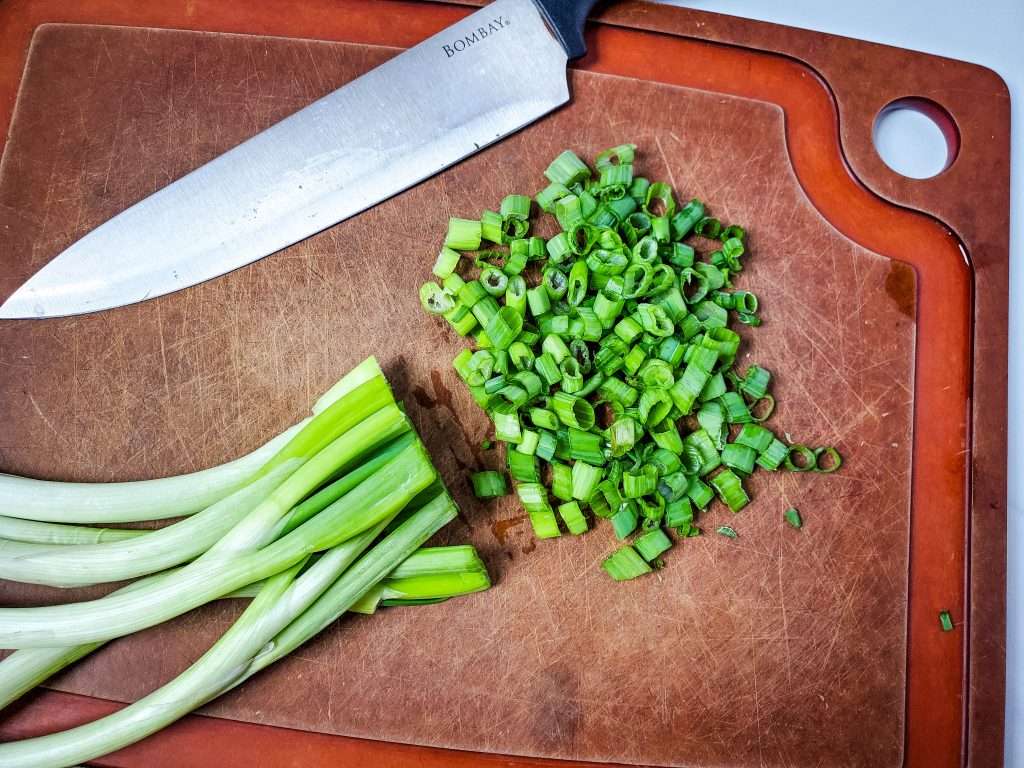 Neiman Marcus Dip 8 chopped green onions on a brown cutting board with knife