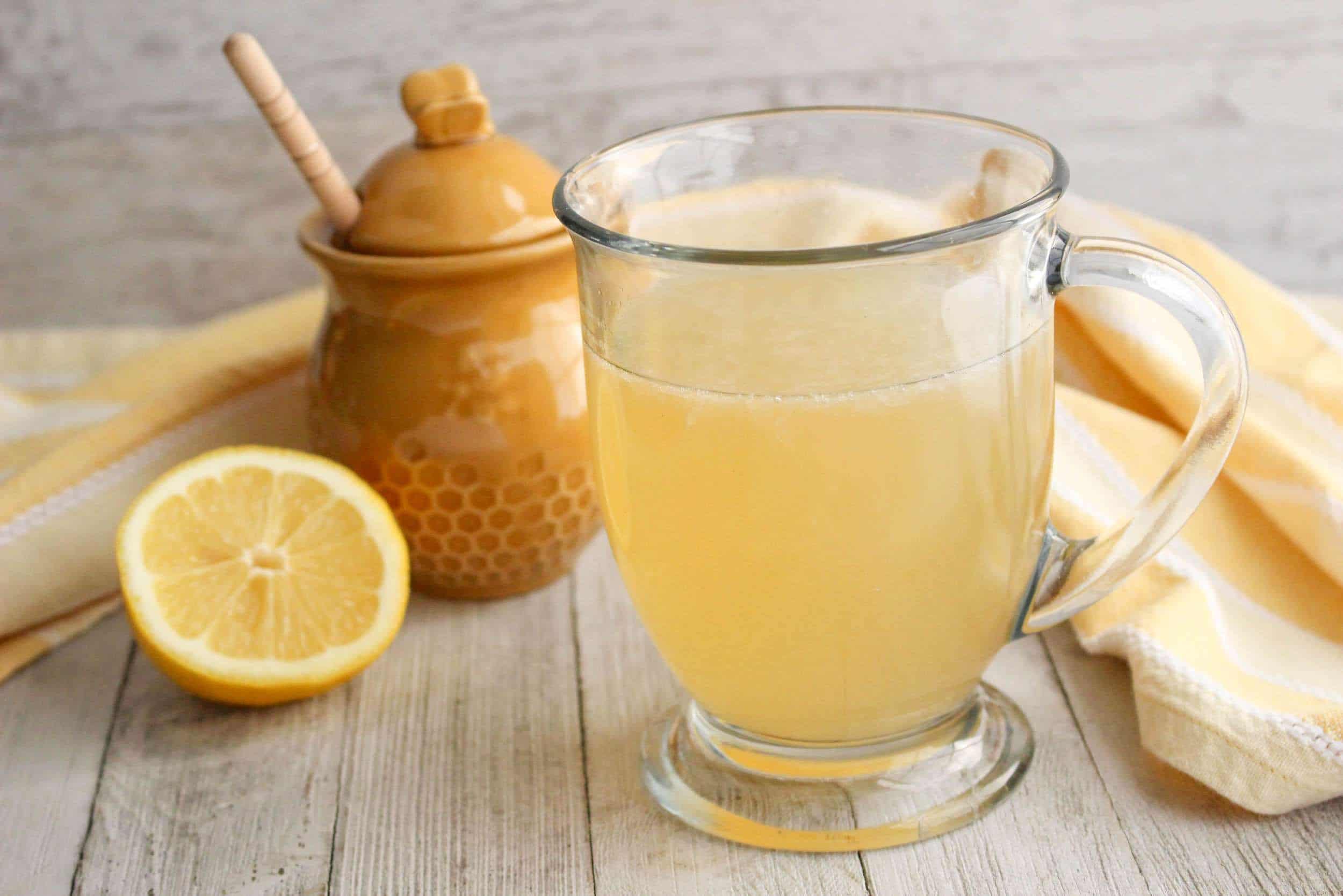 Glass filled with copycat Starbucks Medicine Ball Tea, pot of honey, sliced lemon, cream kitchen cloth in the background.