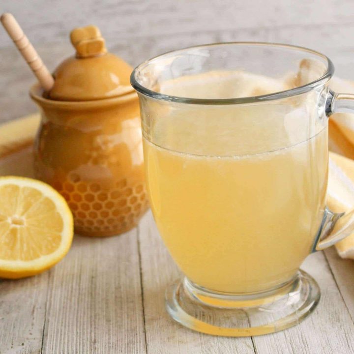 Starbucks Medicine Ball Tea Recipe (Copycat Recipe) 30 Glass filled with copycat Starbucks Medicine Ball, pot of honey, sliced lemon, cream kitchen towel in the background.