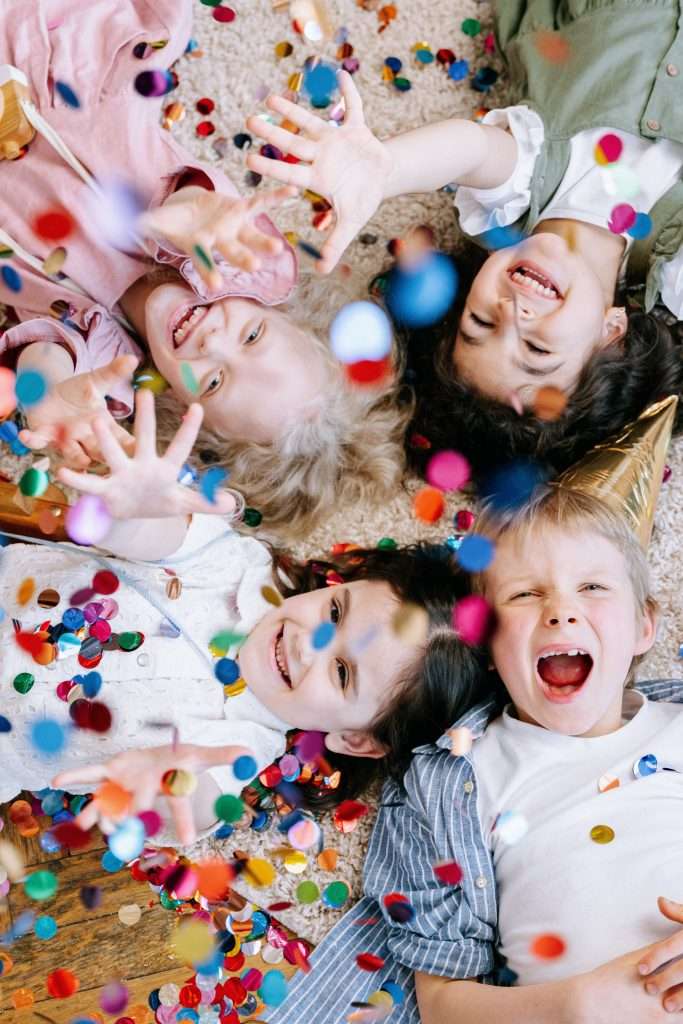 Things to Do with Kids on New Year’s Eve 5 kids celebrating new year's eve with confetti and pom poms