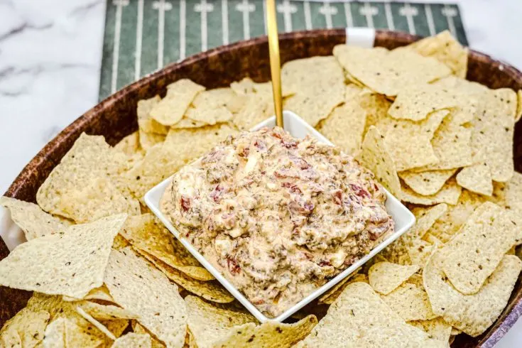 Bowl of Sausage Cheese Dip with serving spoon, surrounded by tortilla chips on a serving platter on a marble countertop.