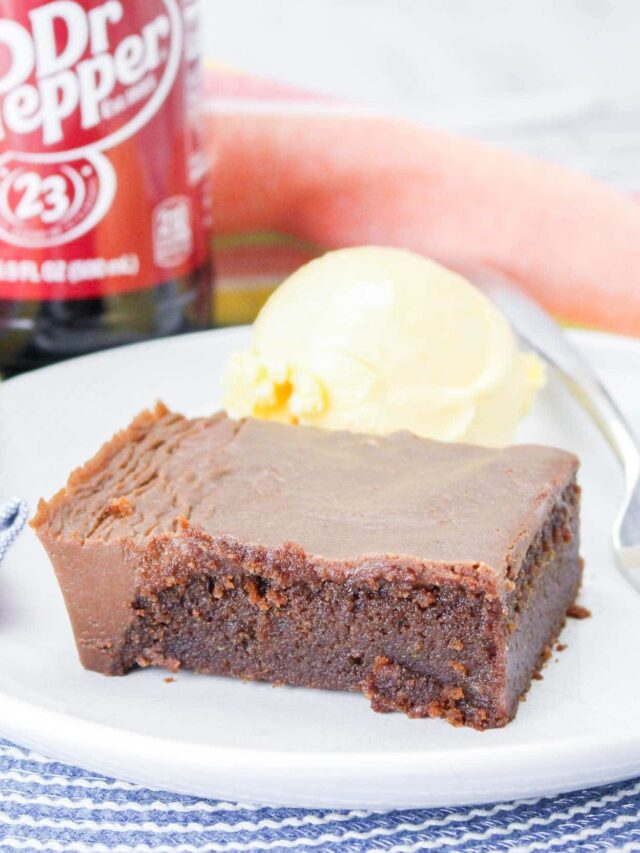 A slice of chocolate cake with a bite taken out, served with a scoop of vanilla ice cream on a white plate. A Dr Pepper bottle is visible in the background.