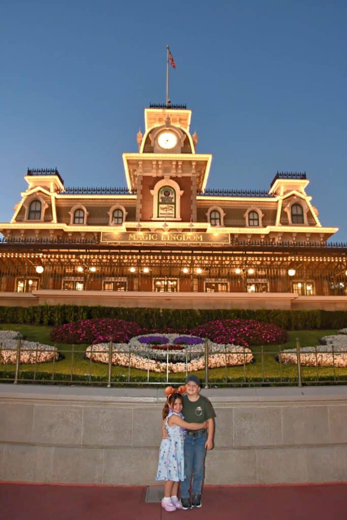 Spring at Disney World: Why This Season Is Pure Enchantment! 4 A little girl on the left hugging a little boy on his side as they stand outside Magic Kingdom's facade. The siblings are photographed outdoors just before nightfall.