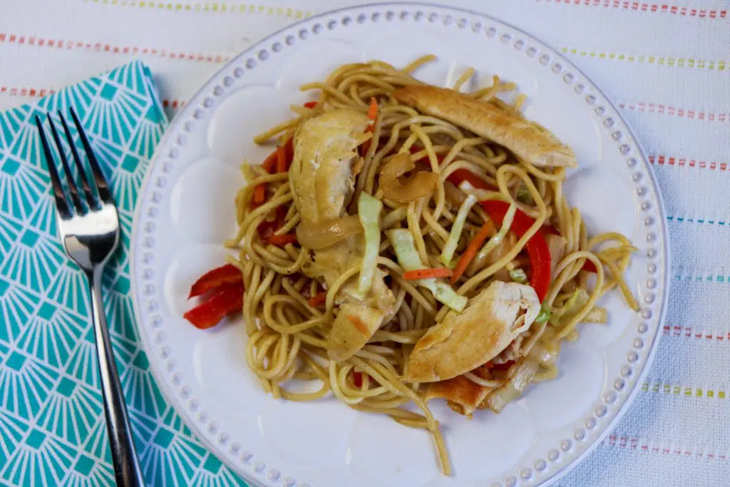 chicken lo mein on white plate with blue napkin beside it 
