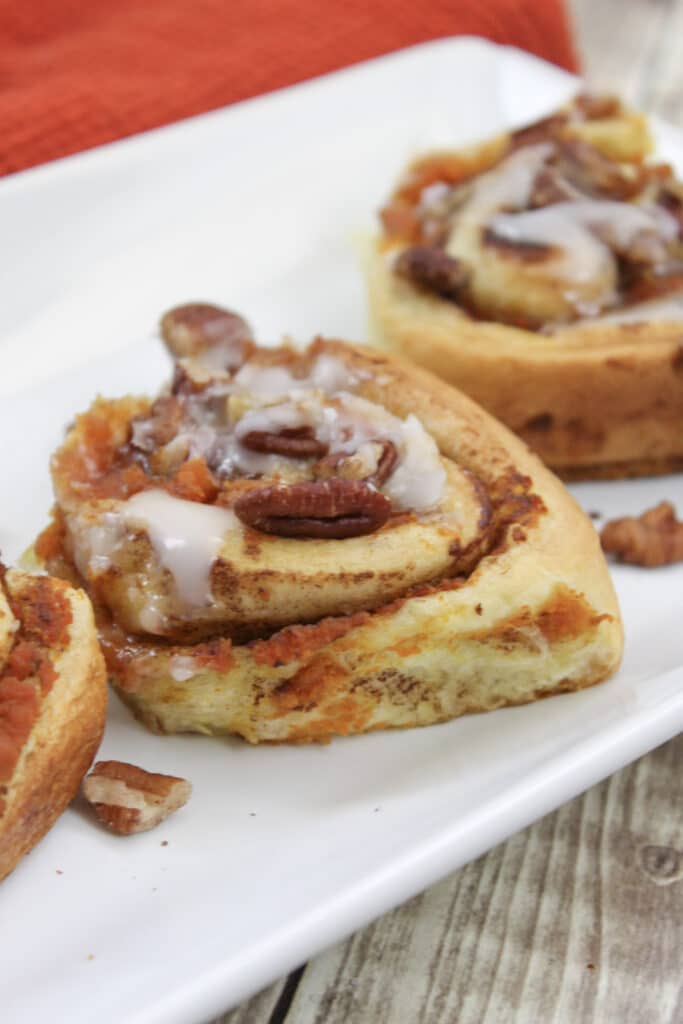 Pumpkin Cinnamon Rolls (3 Ingredients) 7 close up of pumpkin spice cinnamon rolls on white platter.
