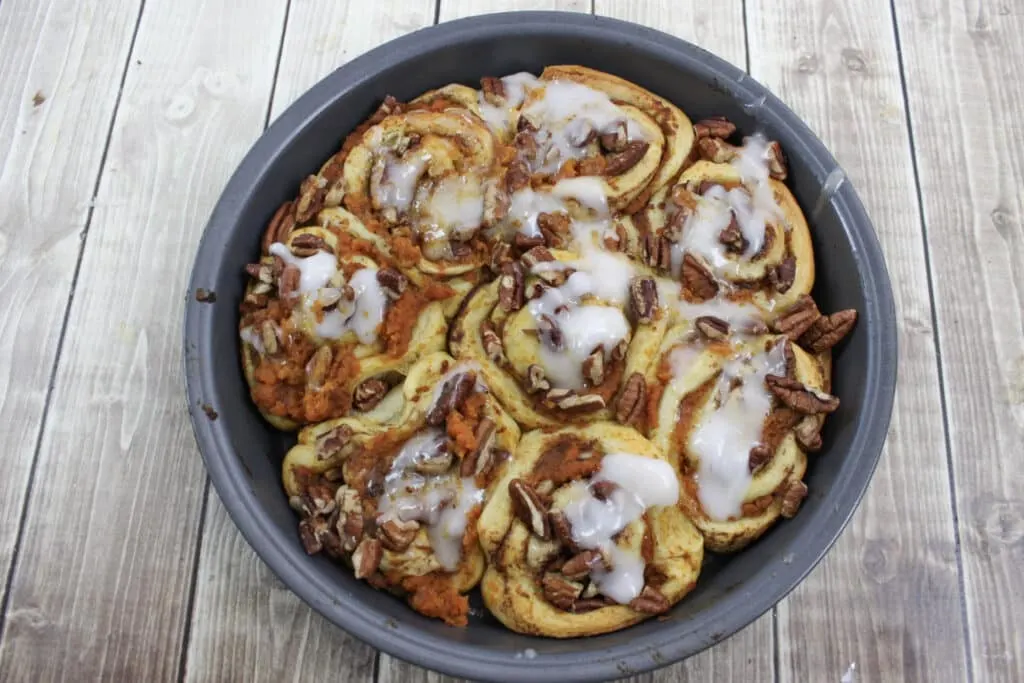 Round pan of pumpkin cinnamon rolls topped with icing and pumpkin spice frosting. 