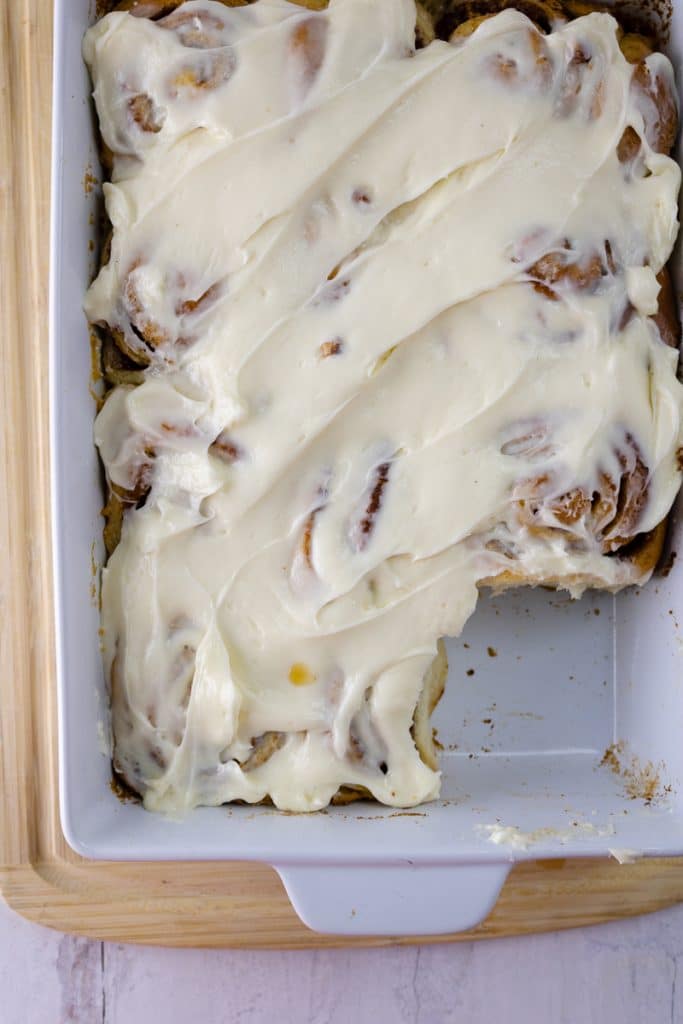 Delicious Apple Pie Cinnamon Rolls Recipe 12 apple pie cinnamon rolls covered with cream cheese in white dish with one taken out