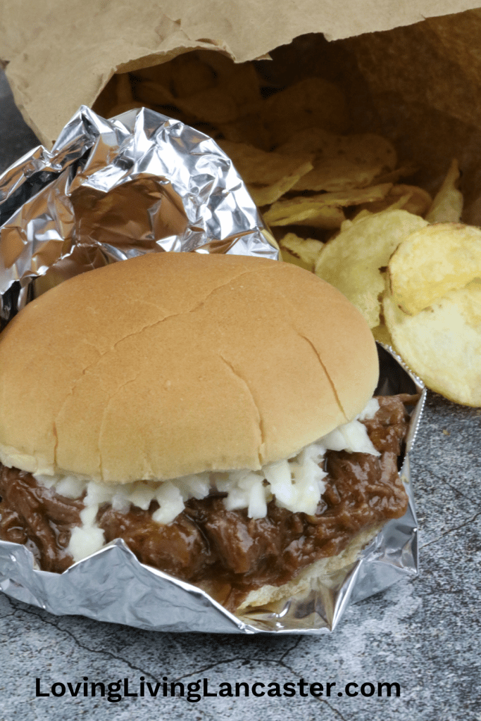 Super Easy Instant Pot Pulled Venison Sandwich 10 A delicious BBQ pulled venison sandwich slider on foil, next to potato chips in a paper bag.