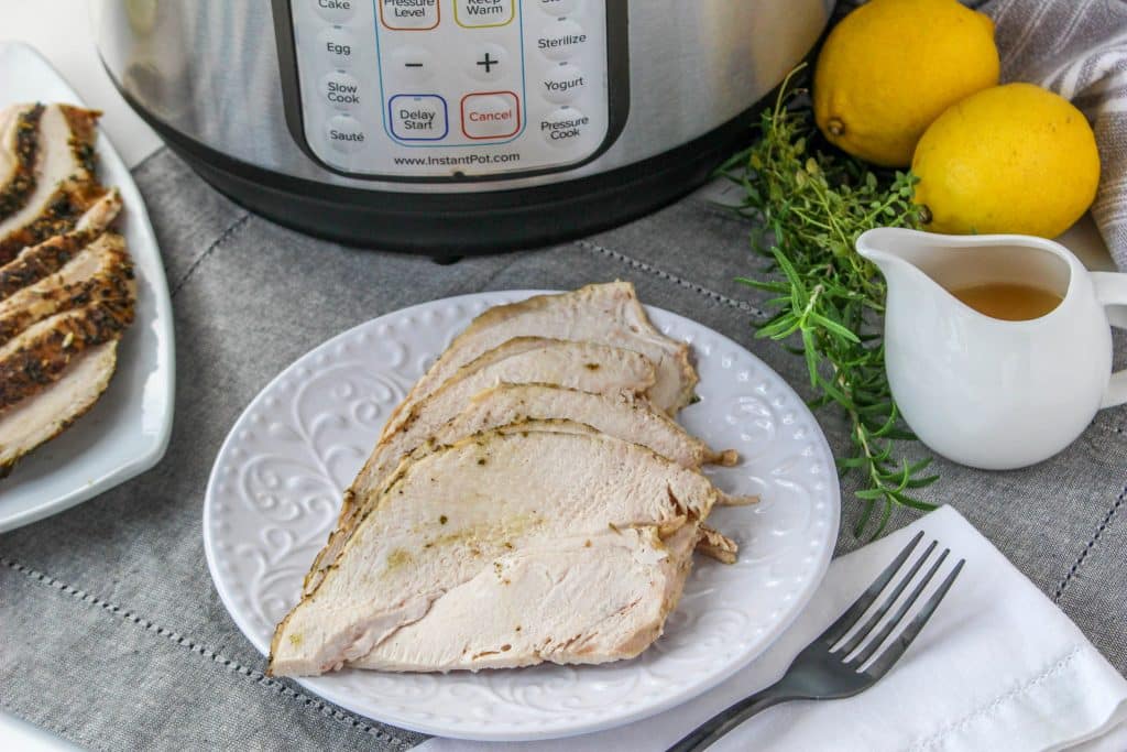 Quick Instant Pot Lemon and Herb Turkey Breast Recipe 8 fully cooked sliced turkey breast on white plate with gravy on side in serving dish