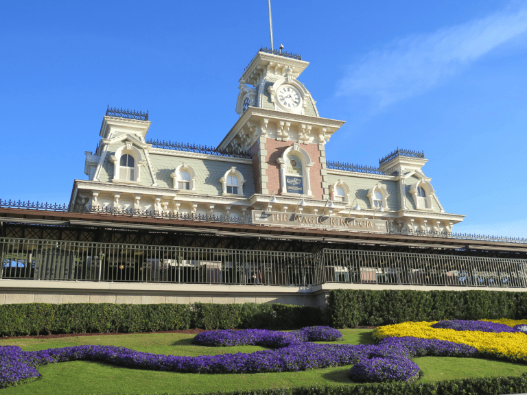 Magic Kingdom Train Station with purple and yellow flowers in front 