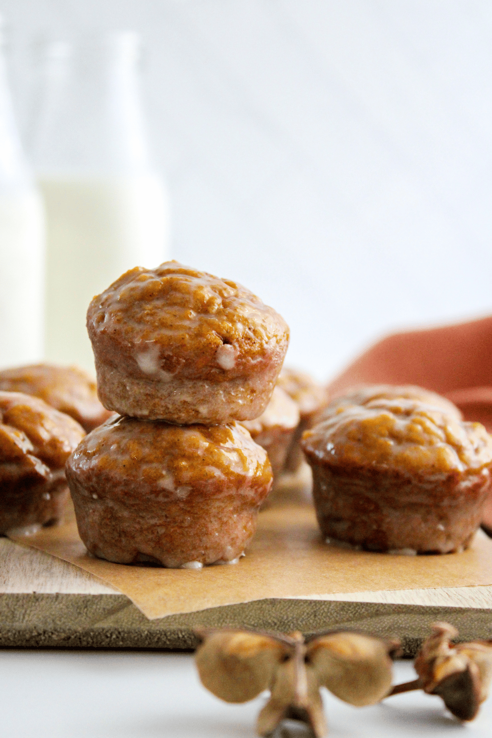 Freshly glazed pumpkin donut holes on a wooden kitchen board, jugs of milk in the background.