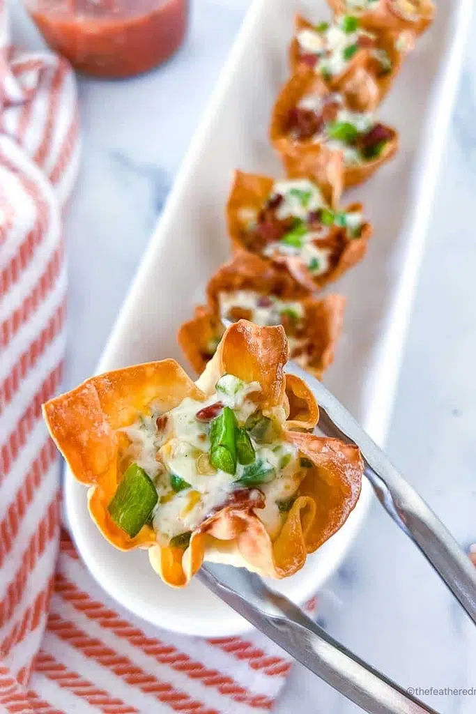 close up of jalapeno popper wonton held by silver tongs 