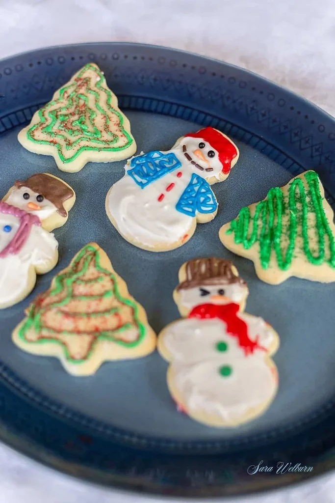 a close up of assorted snowman and Christmas tree cookies on blue plate 