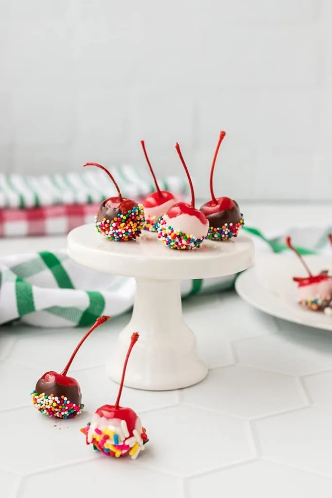 cherries with vanilla and chocolate icing and colorful sprinkles on top of white holder 