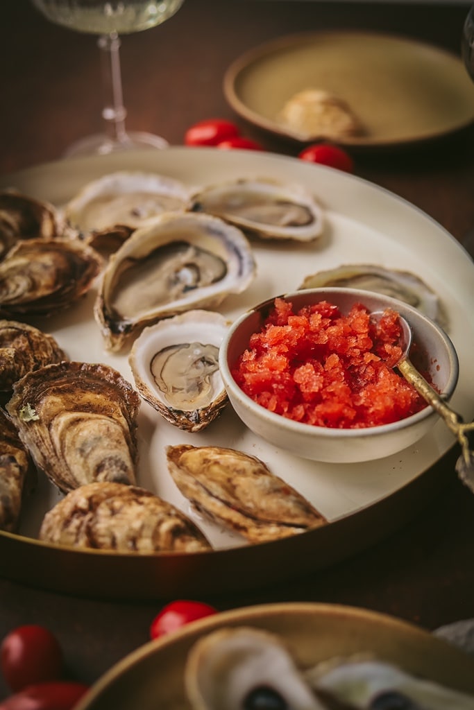 small white serving dish of tomato vermouth with oysters on the side