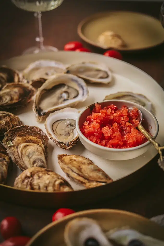 small white serving dish of tomato vermouth with oysters on the side