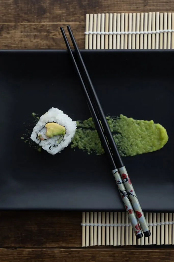 avocado sushi roll with chop sticks and wasabi on side 