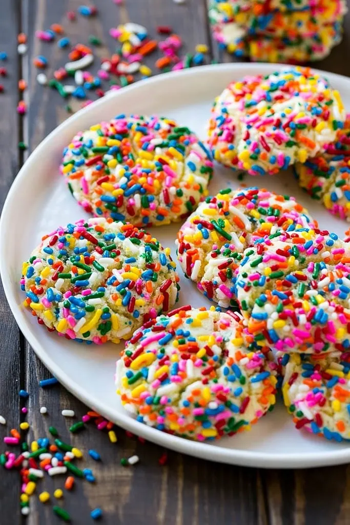 confetti cookies covered in rainbow sprinkles on white plate 