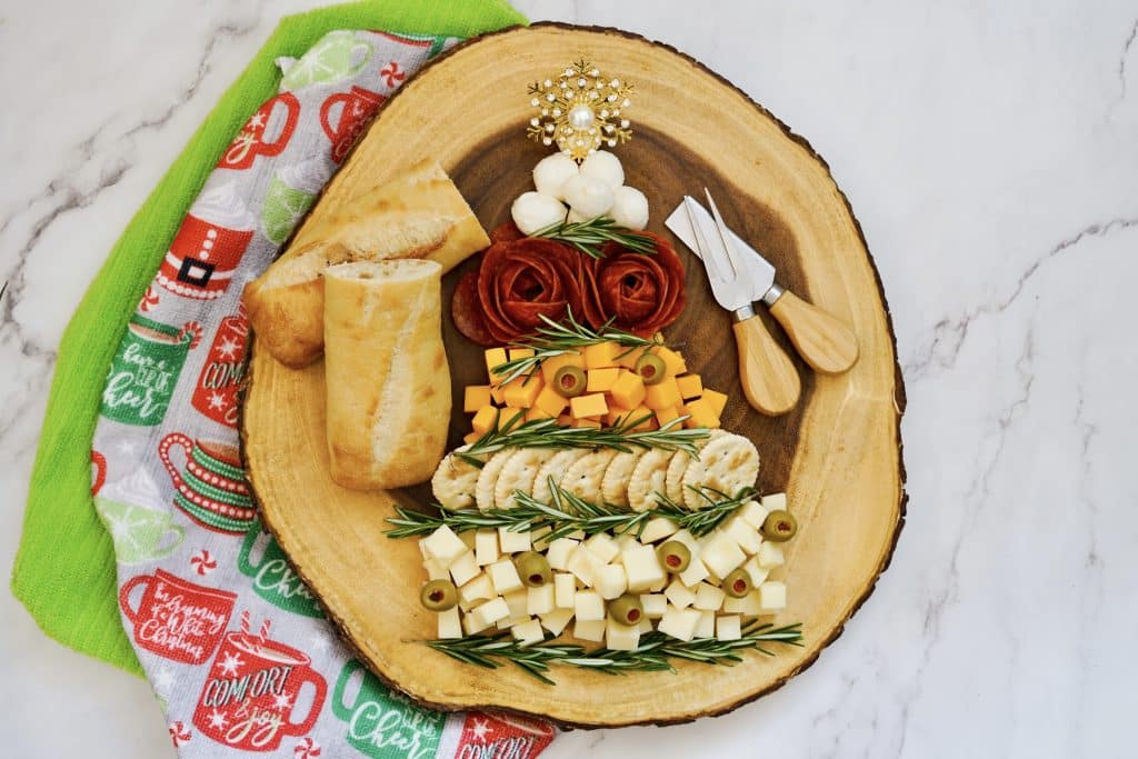 overhead view of meats and cheeses in Christmas tree shape with bread and cheese knife on circular cutting board 