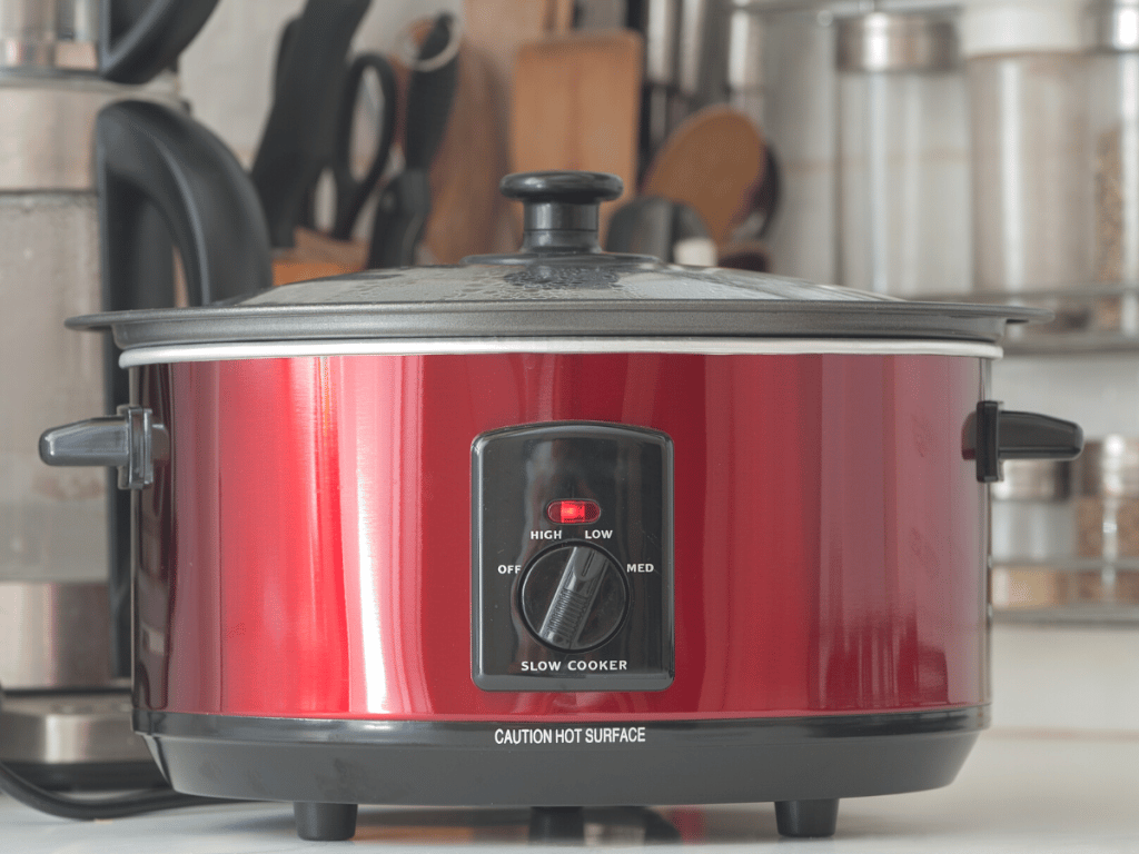 Red slow cooker on countertop with meatballs cooking 