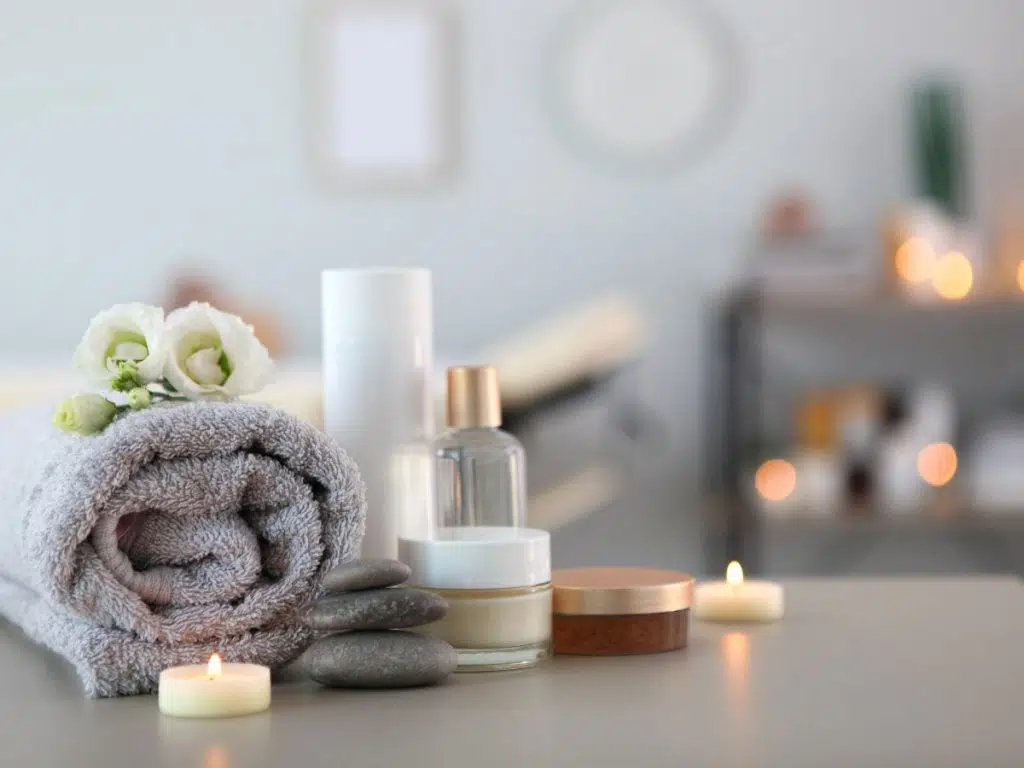 Spa with rolled towel, candles, and flowers on a grey surface.