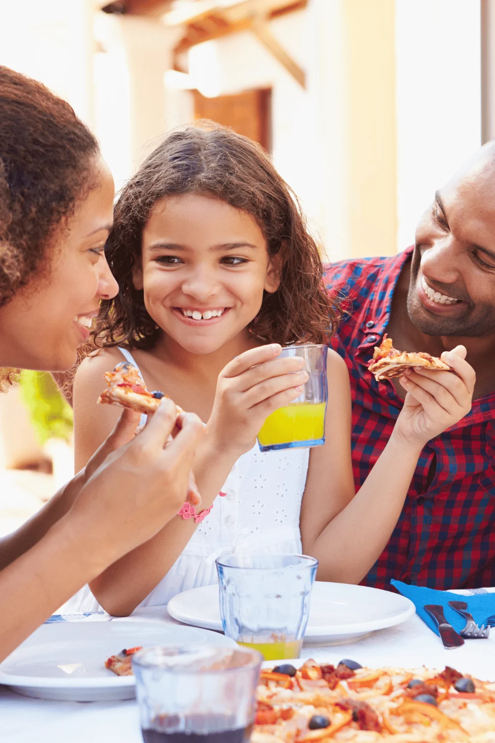 child smiling at mom while holding beverage and food in her hands. Dad is smiling at child next to her. 