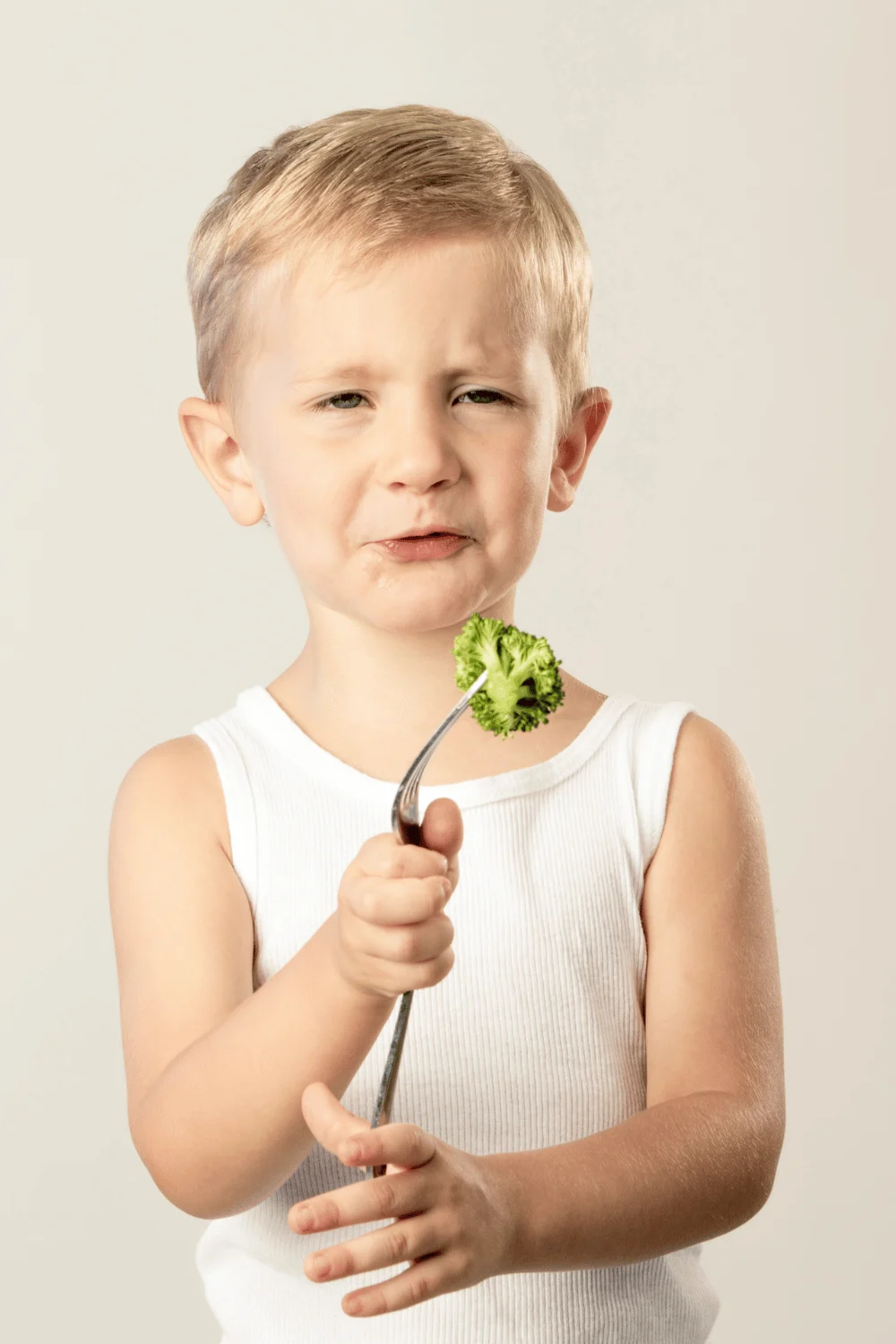 kid holding a piece of broccoli on a fork while making a sad face