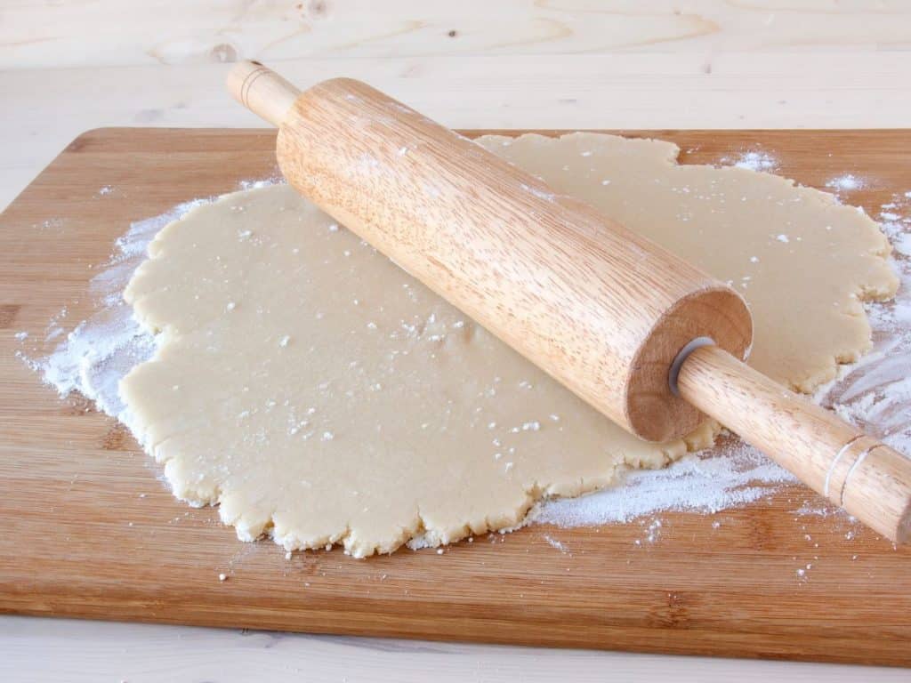 Wooden surface with flour on it and cookie dough rolled out with a rolling pin.