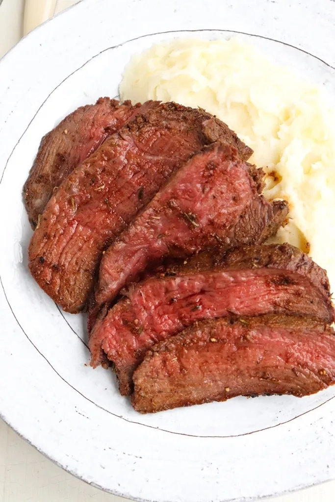 sliced venison backstrap with a side of mashed potatoes on white plate 