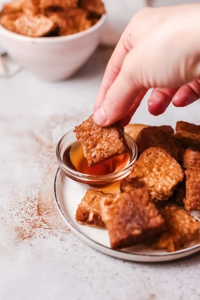 small French toast nuggets getting dipped in clear small bowl of syrup 