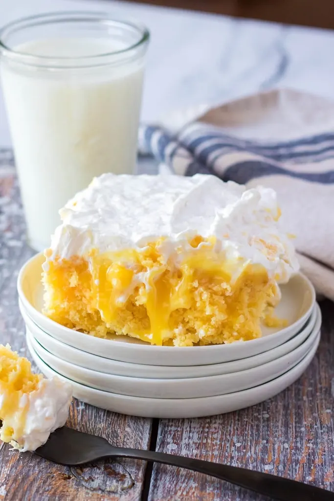 slice of pineapple poke cake with white icing on a stack of white plates