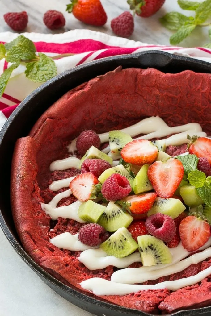 red velvet pancakes in cast iron skillet with strawberries, kiwis and raspberries on top with icing 