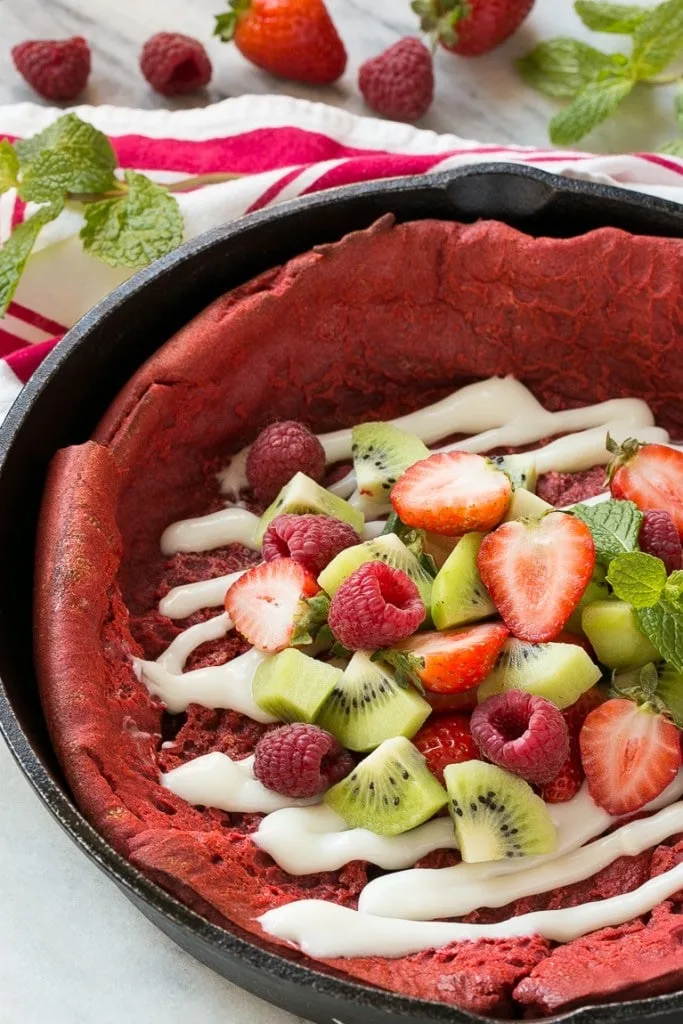 25 Valentine’s Day Breakfast Ideas For Kids 15 red velvet pancakes in cast iron skillet with strawberries, kiwis and raspberries on top with icing