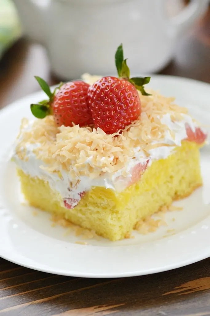 slice of strawberry poke cake with coconut and strawberries on top on white plate 