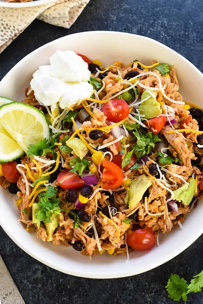 slow cooker chicken thigh burrito bowl with colorful veggies, sour cream, cheese and lime 