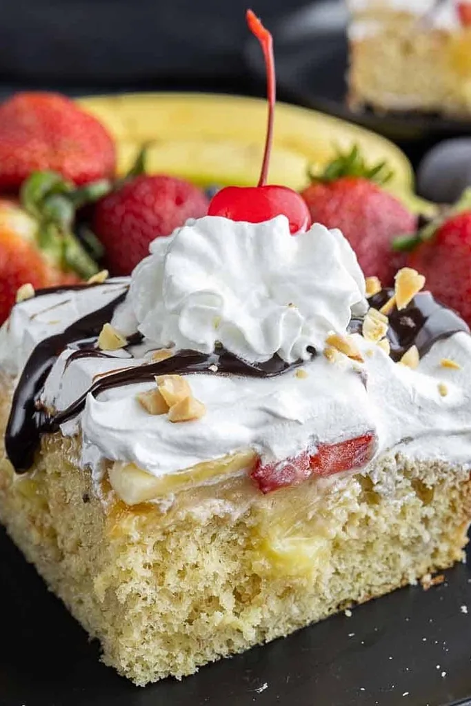 slice of banana split poke cake with cool whip and chocolate drizzle on top 