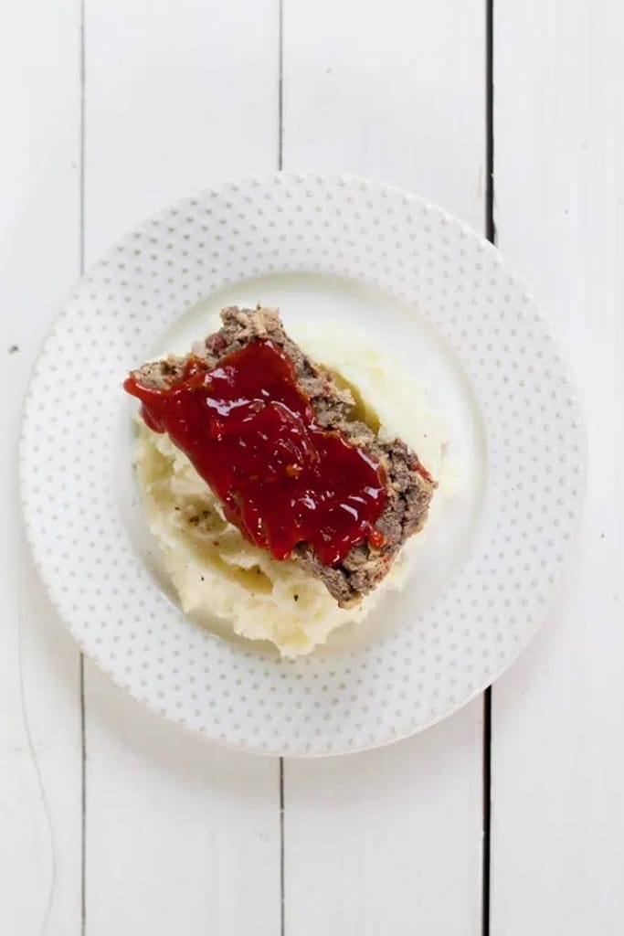 overhead view of Venison Meatloaf with ketchup sauce on mashed potatoes on circle white plate
