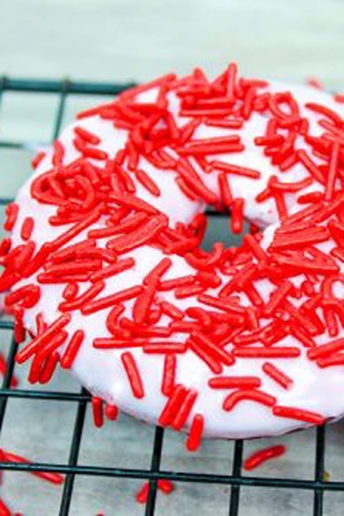 close up of red velvet donuts with white icing and red sprinkles 