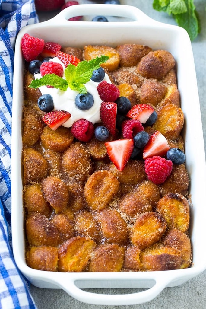 donut breakfast bake with whipped cream and berries in a white casserole dish 