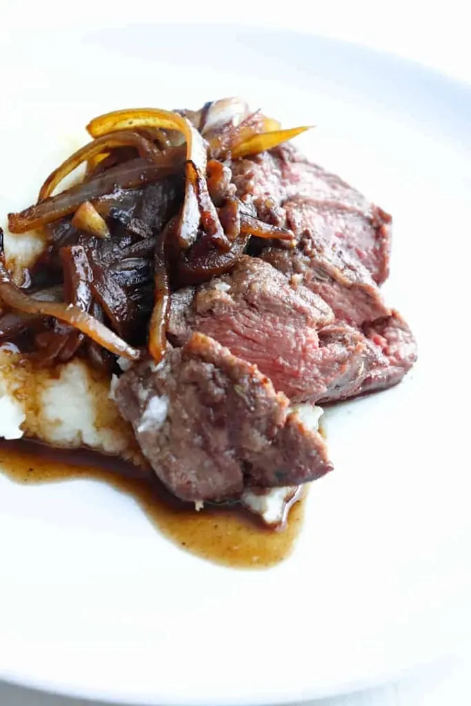 deer meat venison medallions with onions on white plate 