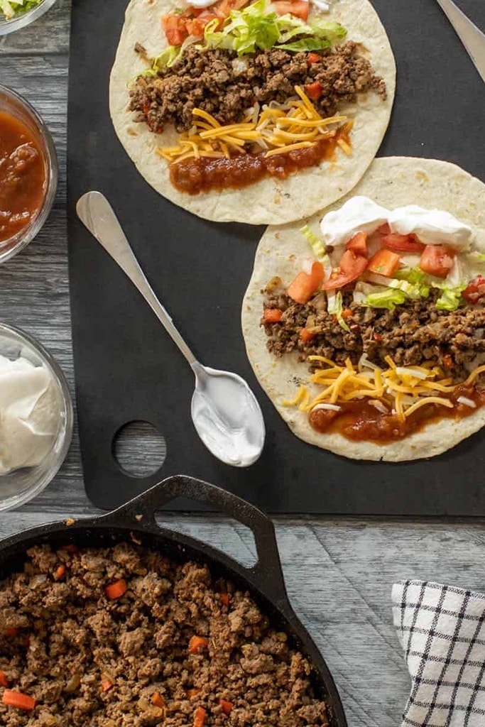 25 Venison Recipes You Will Love 25 deer meat venison tacos with tomatoes, cheese and lettuce on tortillas on black cutting board
