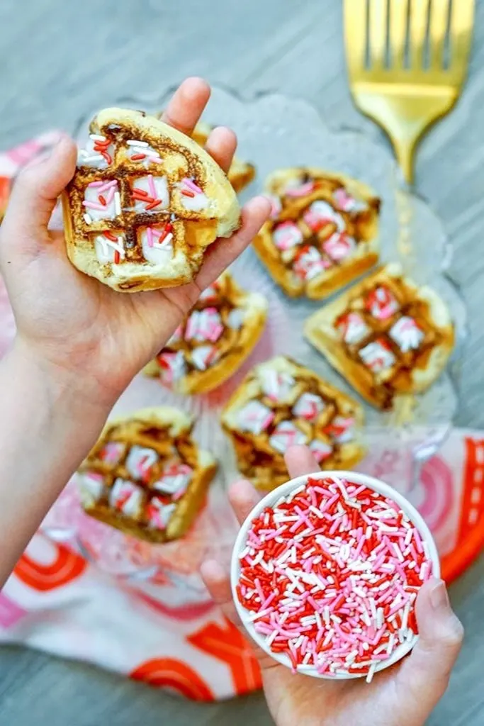 hand holding Valentine's Day cinnamon roll waffles with red and pink sprinkles 