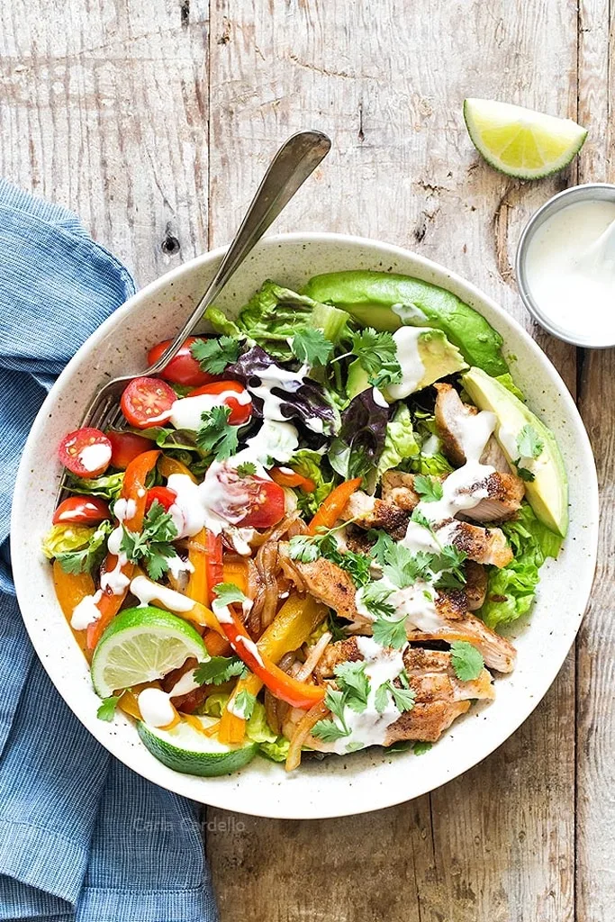 colorful chicken thigh fajita salad with peppers, tomatoes, avocado and lime in white bowl 