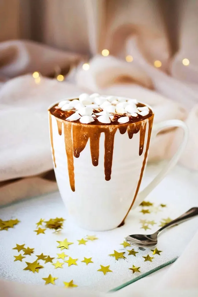 creamy hot chocolate in white mug with chocolate drizzle topped with marshmallows 