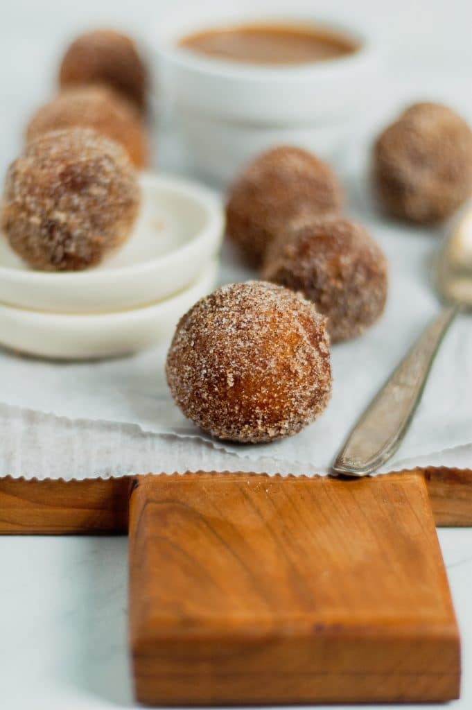 close up of fried cinnamon sugar donut hole on parchment paper and wooden cutting board 