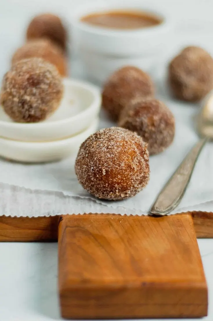 close up of fried cinnamon sugar donut hole on parchment paper and wooden cutting board